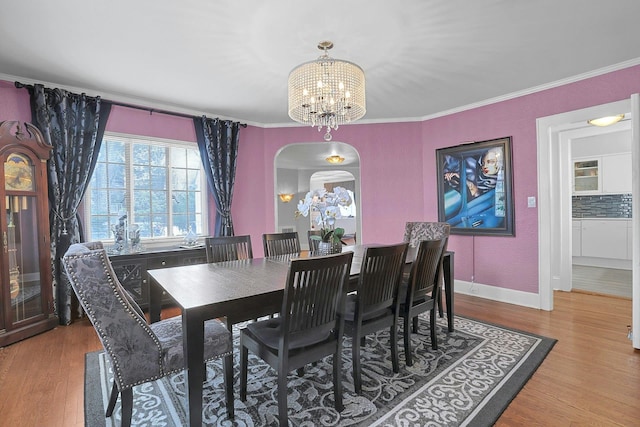 dining area featuring arched walkways, a notable chandelier, wood finished floors, baseboards, and ornamental molding