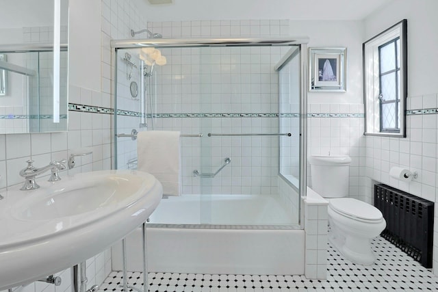 bathroom with bath / shower combo with glass door, radiator, toilet, tile patterned flooring, and tile walls