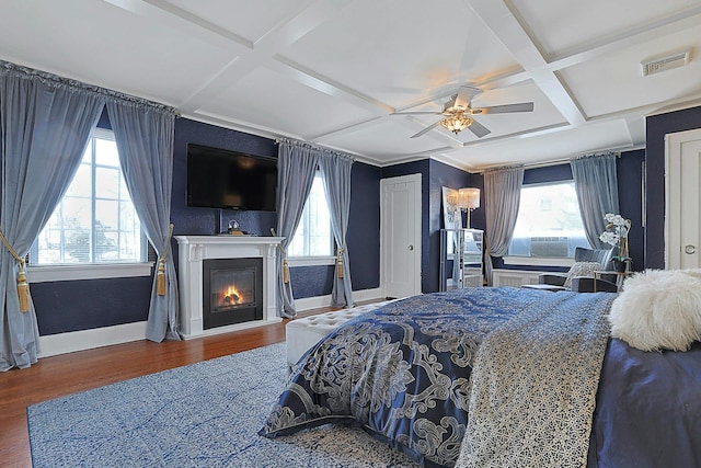 bedroom with a glass covered fireplace, multiple windows, coffered ceiling, and wood finished floors