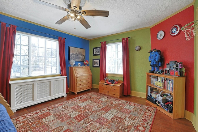 interior space with a textured ceiling, ceiling fan, wood finished floors, baseboards, and radiator