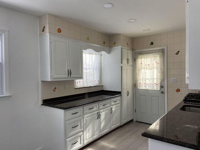 kitchen featuring sink, white cabinetry, light hardwood / wood-style flooring, dark stone counters, and decorative backsplash