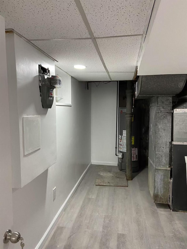 basement with water heater, wood-type flooring, heating unit, and a paneled ceiling