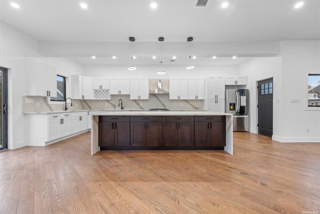 kitchen featuring white cabinetry, a center island, stainless steel refrigerator with ice dispenser, wall chimney exhaust hood, and light wood-type flooring