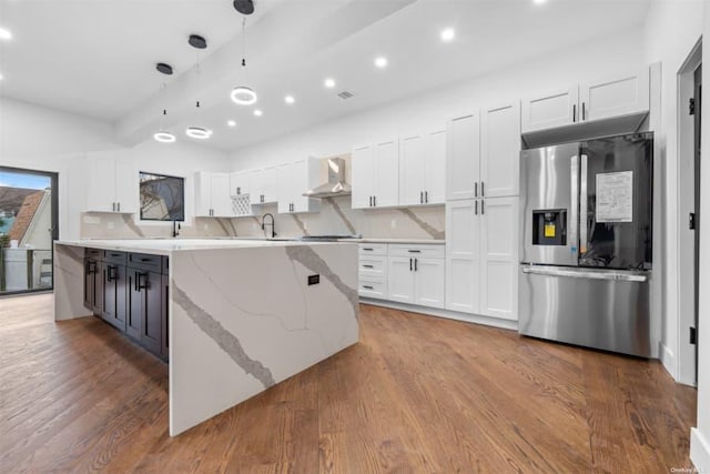 kitchen featuring hanging light fixtures, stainless steel refrigerator with ice dispenser, white cabinets, a kitchen island, and wall chimney exhaust hood