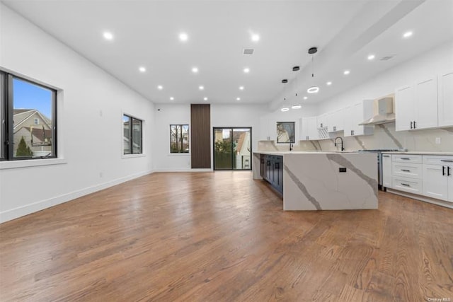 kitchen with white cabinetry, wall chimney range hood, light stone countertops, and light wood-type flooring