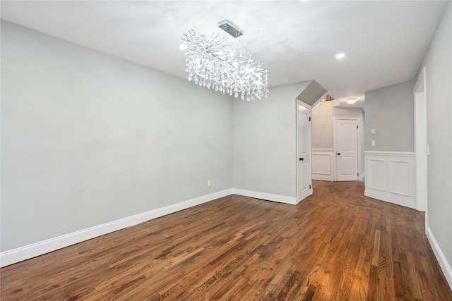 spare room with dark hardwood / wood-style floors and an inviting chandelier