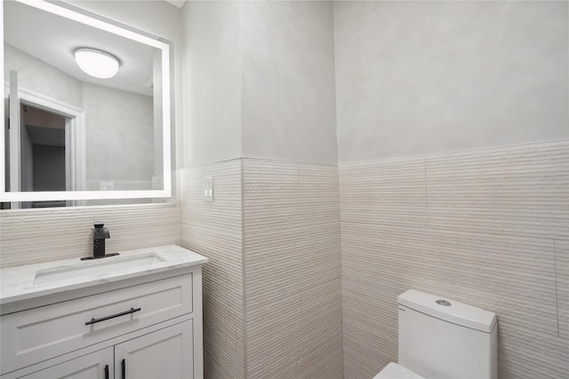 bathroom with vanity, toilet, and tile walls