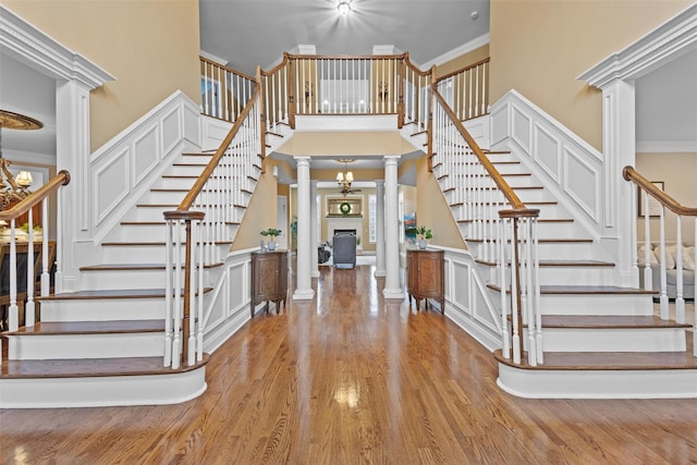 foyer entrance featuring ornate columns, a towering ceiling, light wood-type flooring, crown molding, and an inviting chandelier