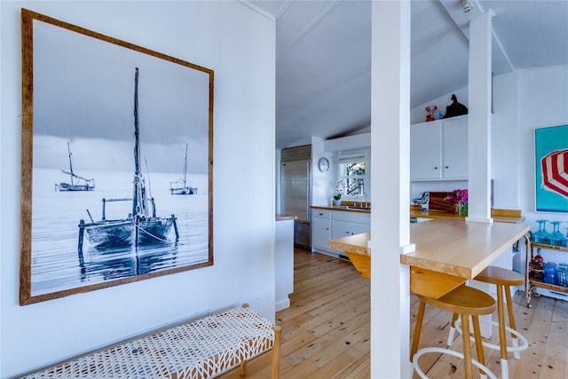 interior space featuring white cabinets, vaulted ceiling, built in refrigerator, and light wood finished floors