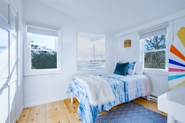 bedroom with vaulted ceiling, baseboard heating, and light wood-style floors