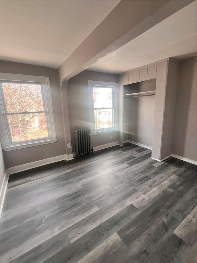 unfurnished bedroom with dark wood-type flooring, radiator heating unit, baseboards, and a closet