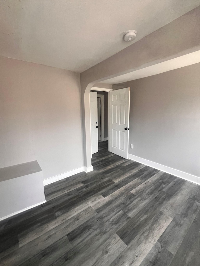 spare room featuring arched walkways, dark wood-type flooring, and baseboards