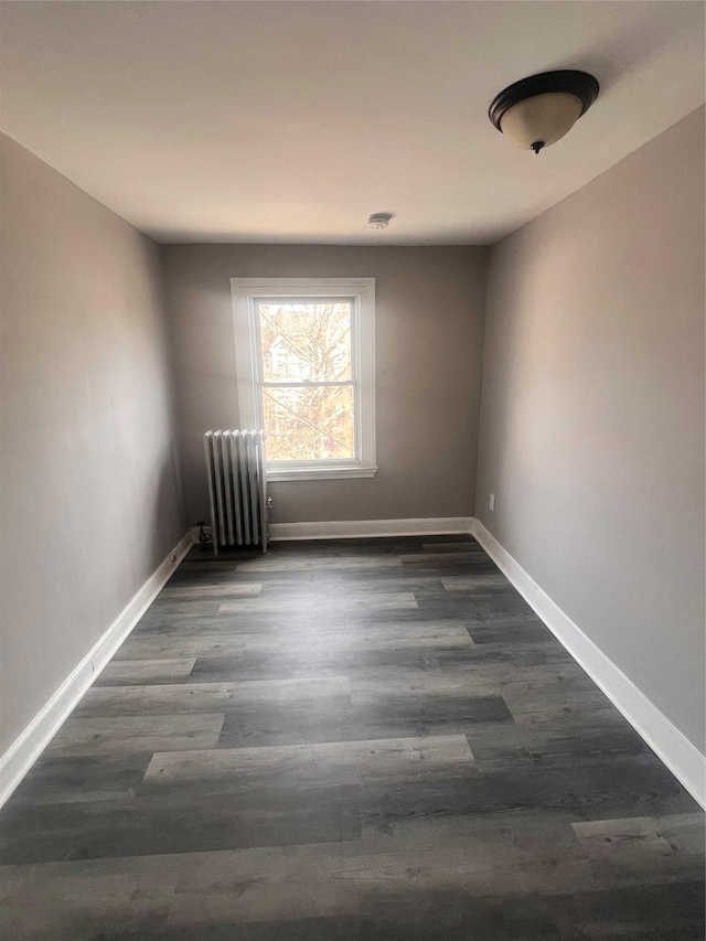 unfurnished room featuring baseboards, dark wood-style flooring, and radiator heating unit