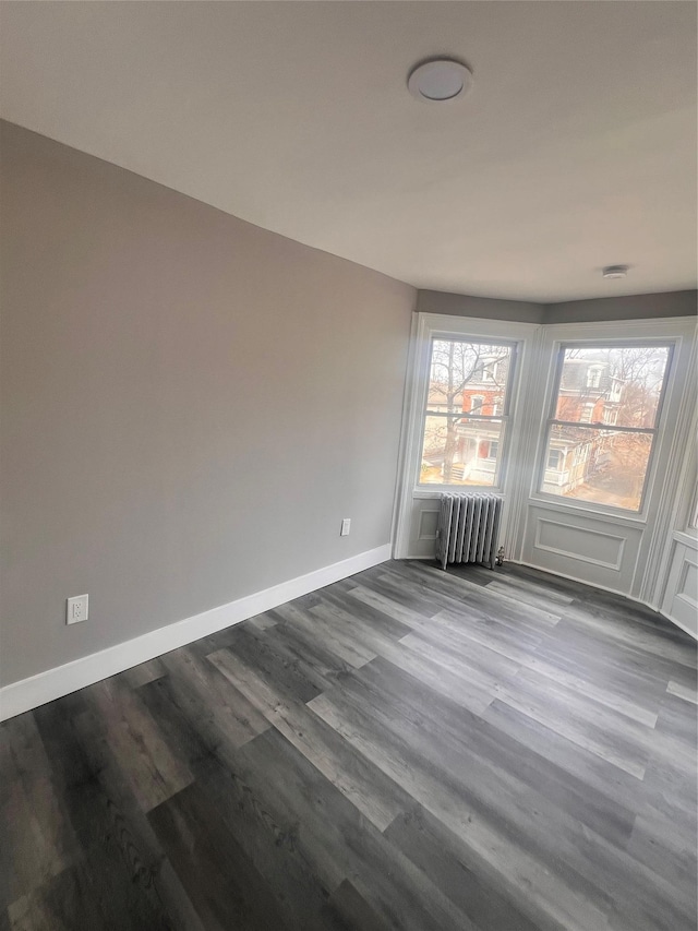 spare room with radiator heating unit, baseboards, and dark wood-style flooring