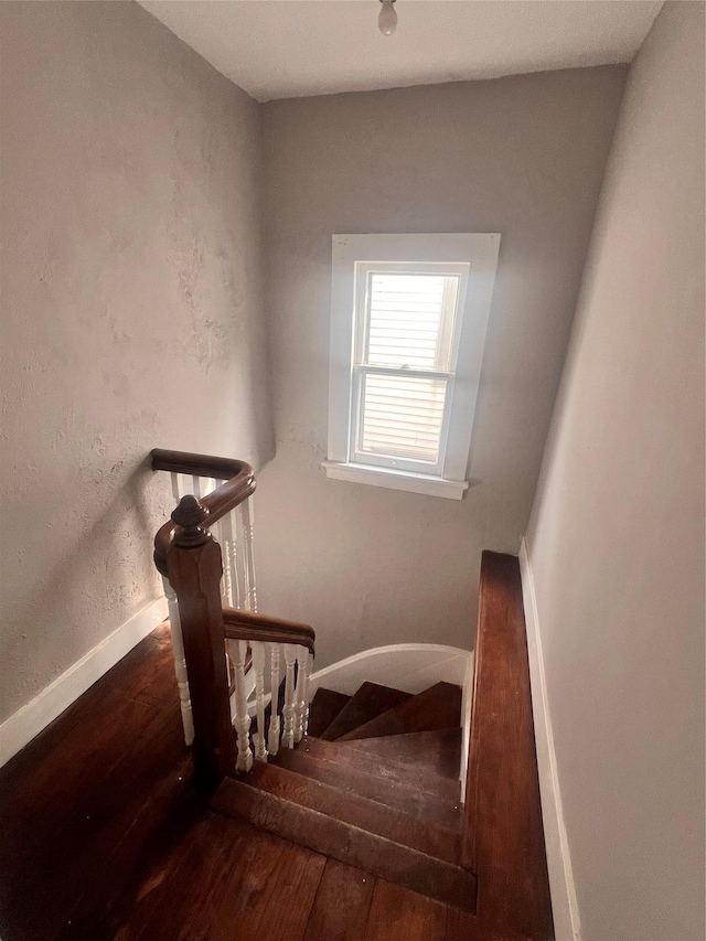 stairway featuring wood finished floors, baseboards, and a textured wall