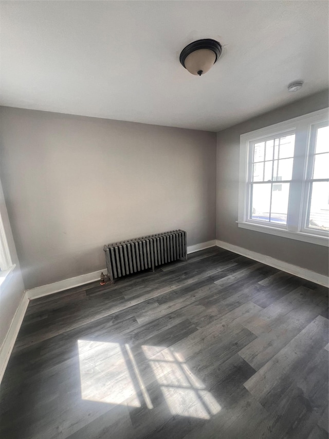 spare room with radiator heating unit, baseboards, and wood finished floors