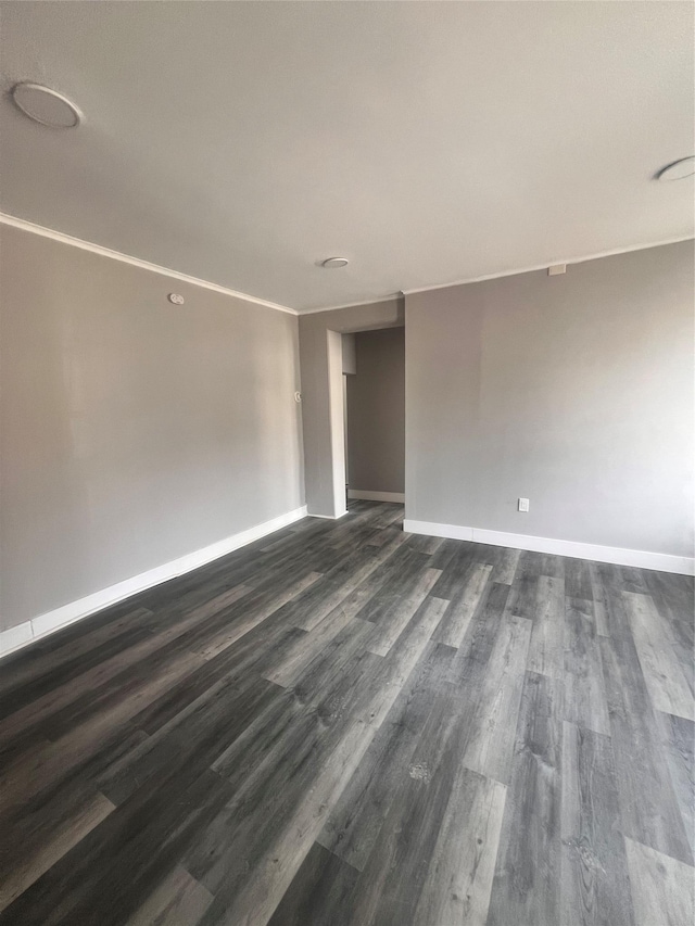 empty room with crown molding, baseboards, and dark wood-style flooring