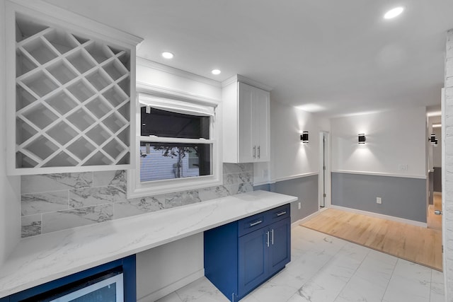 kitchen featuring tasteful backsplash, blue cabinetry, white cabinets, and light stone counters