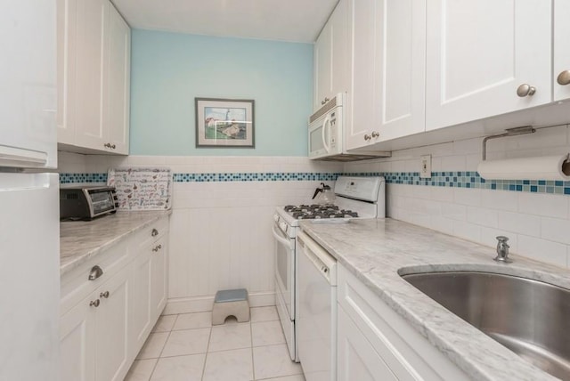 kitchen featuring white appliances, white cabinets, a wainscoted wall, light stone countertops, and light tile patterned flooring