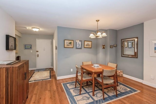 dining room with light wood-style floors, a notable chandelier, and baseboards