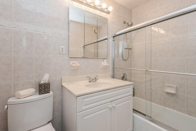 full bath with toilet, shower / bath combination with glass door, vanity, and tile walls