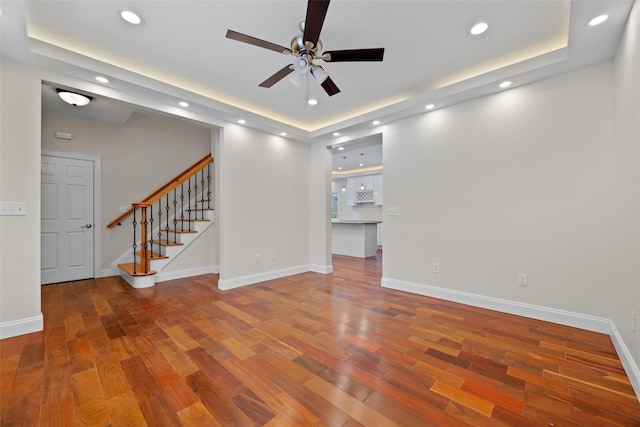 unfurnished living room featuring wood-type flooring, ceiling fan, and a tray ceiling