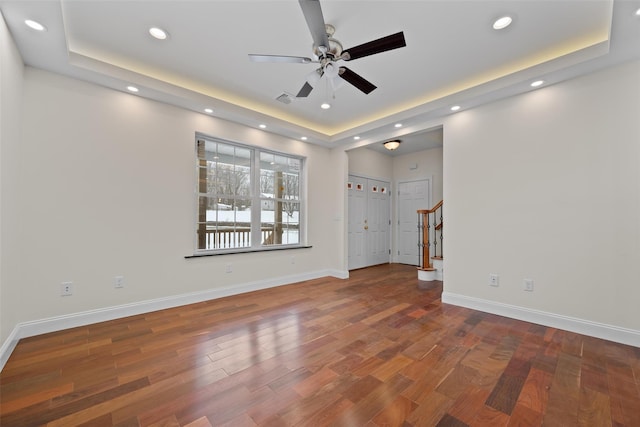 unfurnished living room with dark hardwood / wood-style floors, ceiling fan, and a tray ceiling