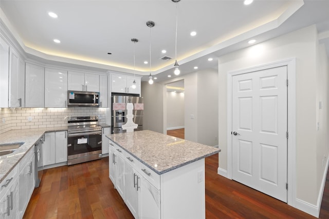 kitchen with dark wood-type flooring, hanging light fixtures, appliances with stainless steel finishes, a kitchen island, and white cabinets