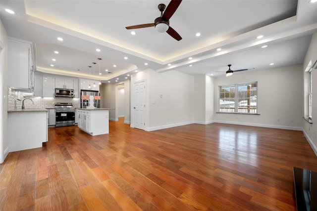 unfurnished living room with a raised ceiling, sink, hardwood / wood-style floors, and ceiling fan