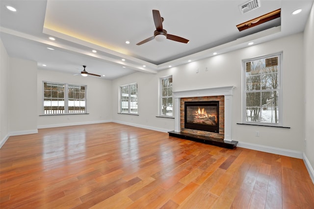 unfurnished living room featuring a tray ceiling, ceiling fan, and light wood-type flooring