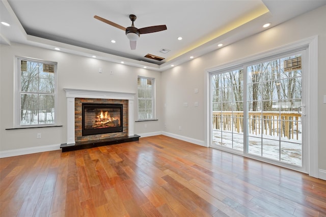 unfurnished living room with a raised ceiling, ceiling fan, and light hardwood / wood-style flooring