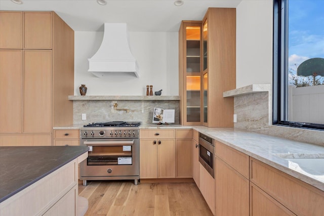 kitchen with stainless steel appliances, tasteful backsplash, light stone countertops, light brown cabinetry, and custom exhaust hood