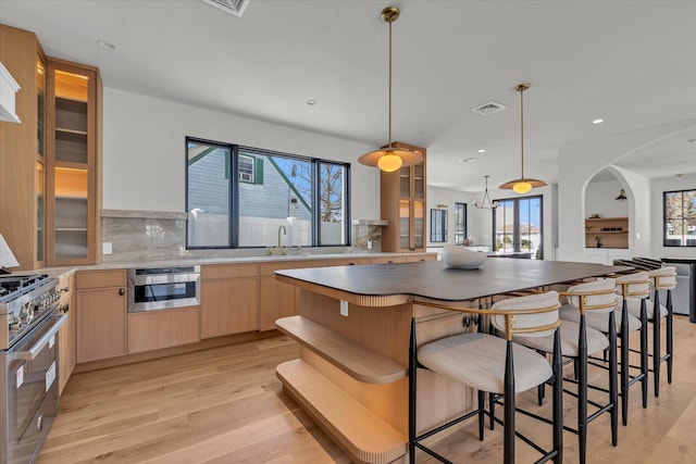 kitchen with a center island, light brown cabinets, pendant lighting, stainless steel appliances, and decorative backsplash