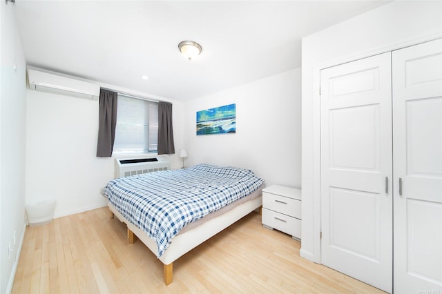 bedroom featuring a wall mounted air conditioner, light hardwood / wood-style floors, and a closet