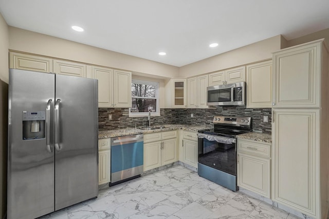 kitchen featuring sink, light stone counters, appliances with stainless steel finishes, decorative backsplash, and cream cabinetry