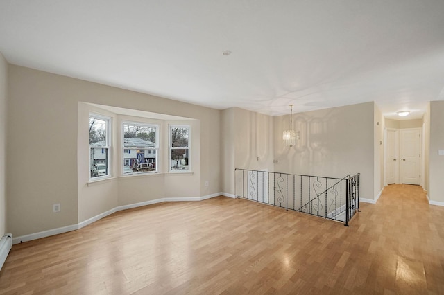 spare room featuring a baseboard heating unit, a notable chandelier, and light wood-type flooring