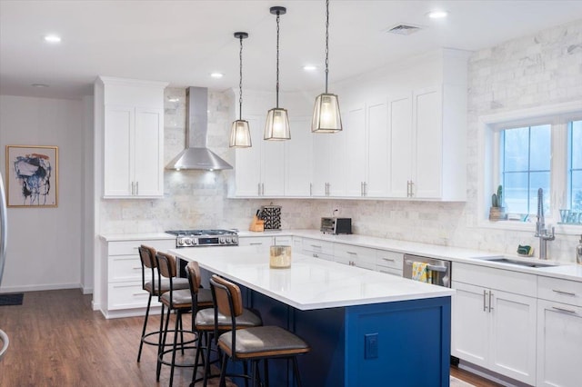 kitchen featuring sink, appliances with stainless steel finishes, white cabinetry, a kitchen island, and wall chimney exhaust hood