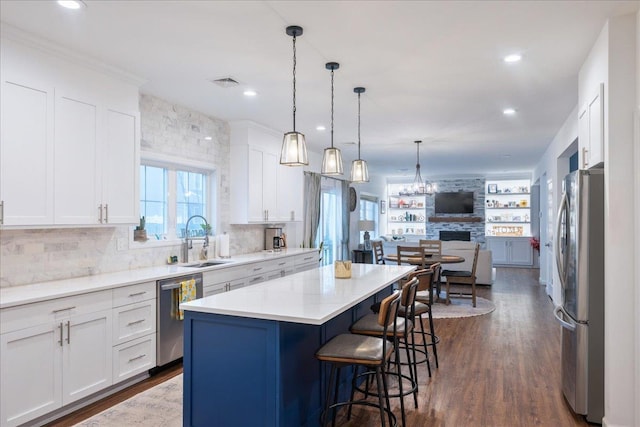 kitchen featuring sink, appliances with stainless steel finishes, a kitchen island, pendant lighting, and white cabinets