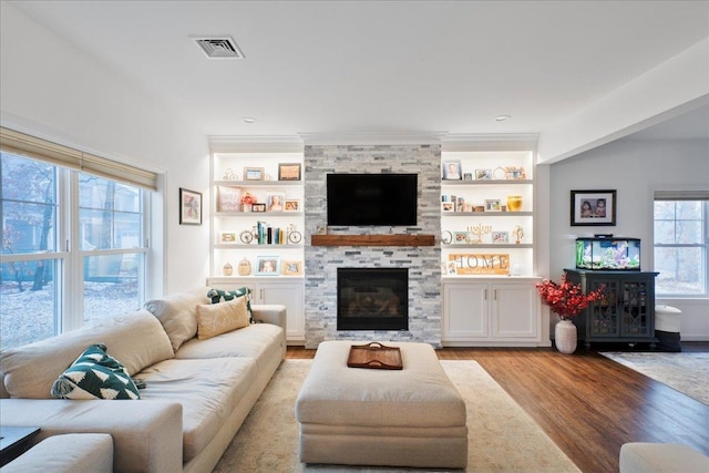 living room with a stone fireplace, light hardwood / wood-style floors, and built in shelves