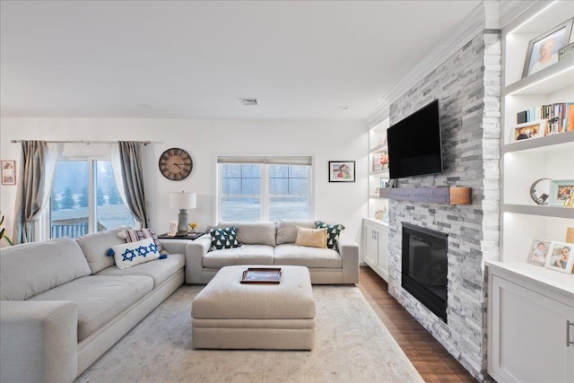 living room featuring hardwood / wood-style flooring, plenty of natural light, built in features, and a stone fireplace