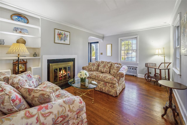 living room featuring dark hardwood / wood-style flooring, built in shelves, radiator heating unit, and ornamental molding