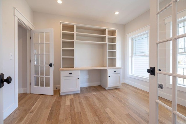 unfurnished office with french doors, built in desk, and light wood-type flooring