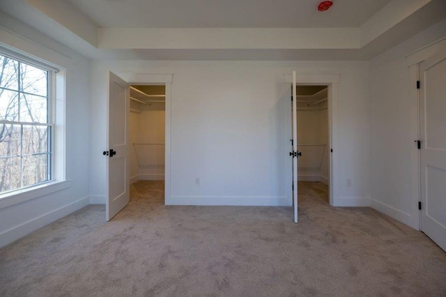 unfurnished bedroom with light colored carpet, a spacious closet, and multiple windows