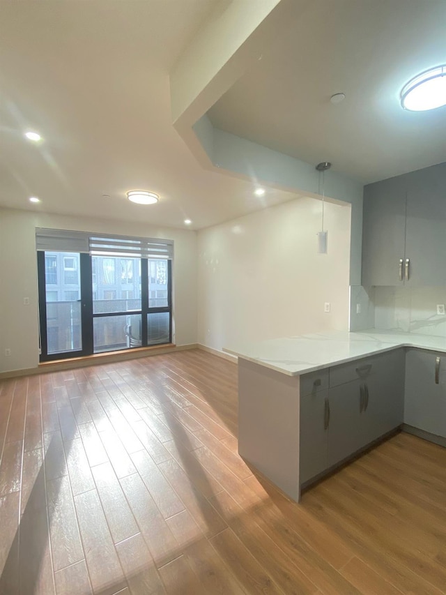 kitchen featuring gray cabinetry, tasteful backsplash, decorative light fixtures, light wood-type flooring, and kitchen peninsula