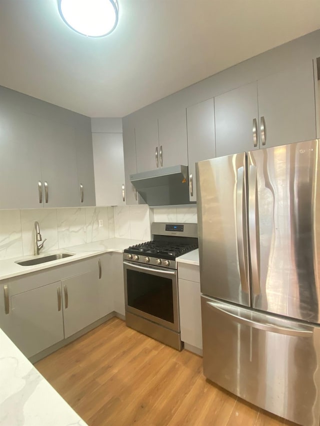 kitchen with appliances with stainless steel finishes, ventilation hood, sink, decorative backsplash, and light hardwood / wood-style flooring