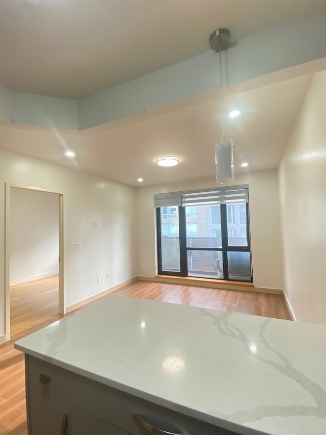 kitchen featuring light stone counters, decorative light fixtures, and light hardwood / wood-style flooring