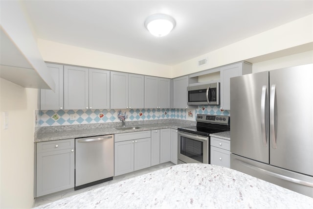 kitchen featuring sink, gray cabinetry, stainless steel appliances, tasteful backsplash, and light stone countertops