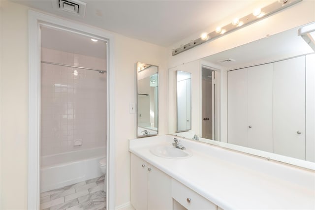 full bathroom featuring tiled shower / bath, vanity, and toilet