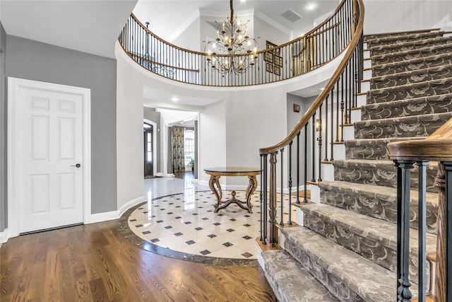 foyer entrance with an inviting chandelier, crown molding, wood-type flooring, and a high ceiling