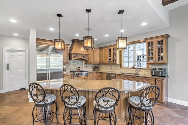 kitchen featuring premium range hood, appliances with stainless steel finishes, pendant lighting, sink, and a large island